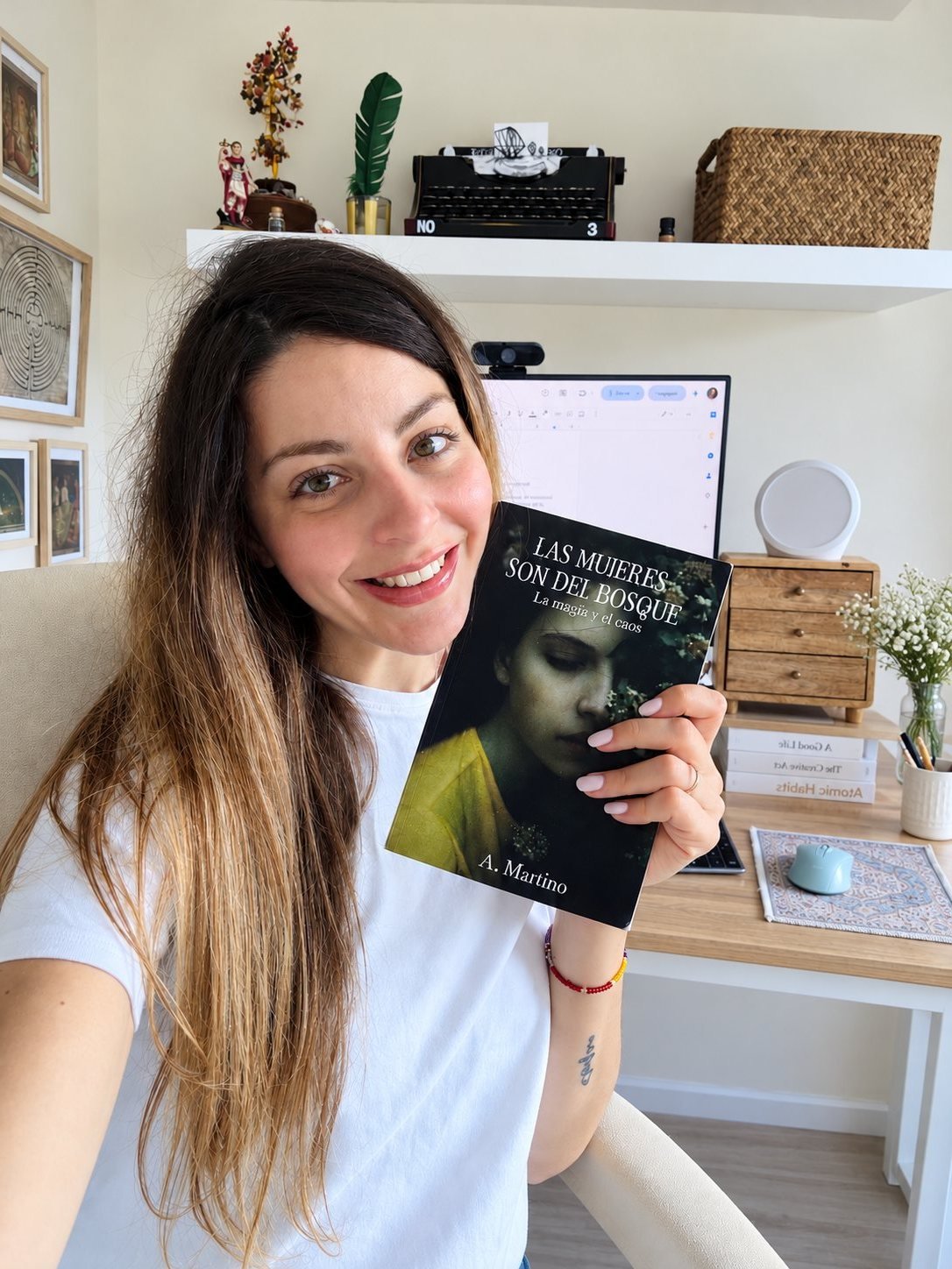 Alex Martino holding her book Las mujeres son del bosque at her writing desk