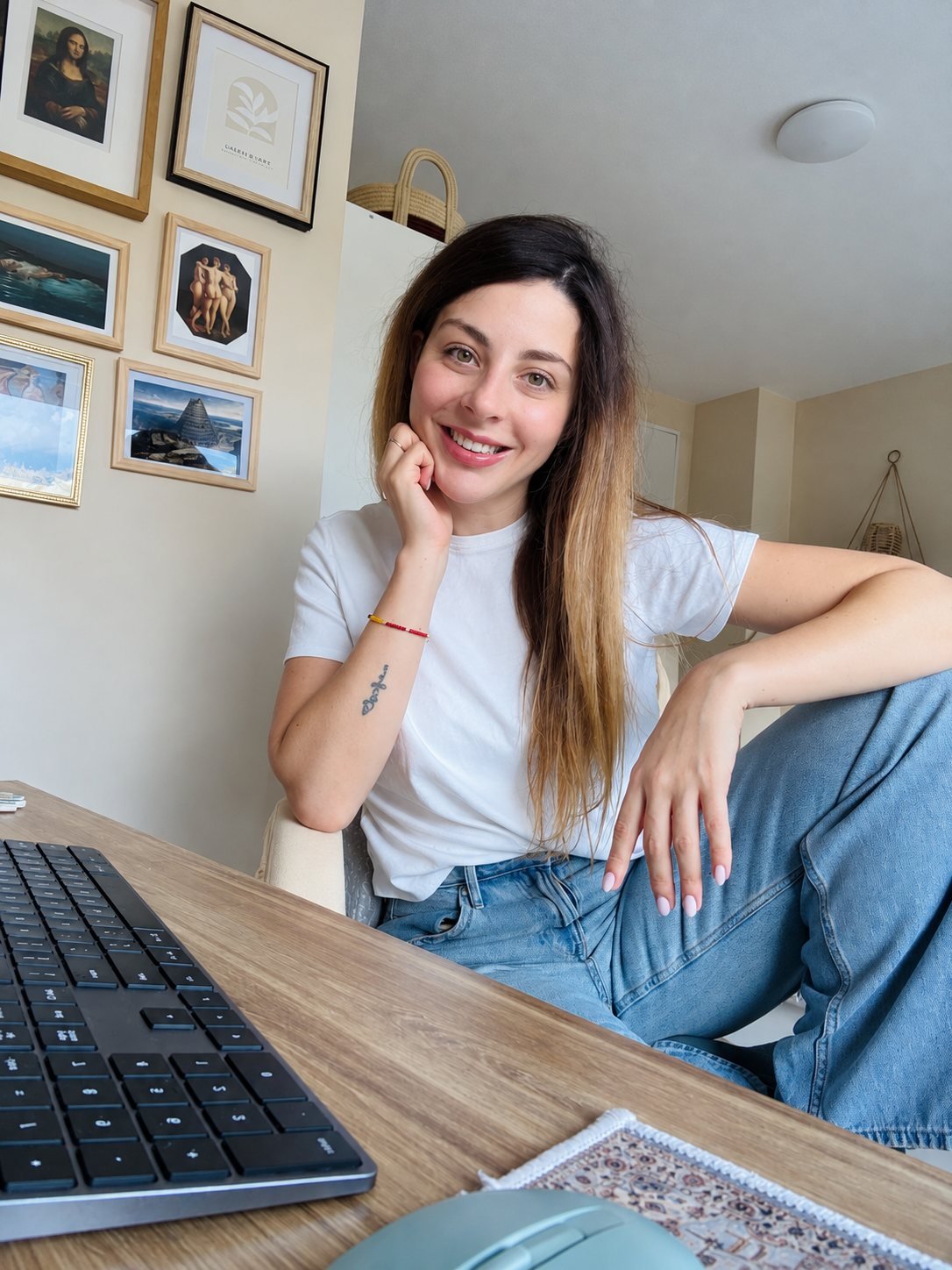 Alex Martino smiling at her writing desk in front of a wall of framed art prints